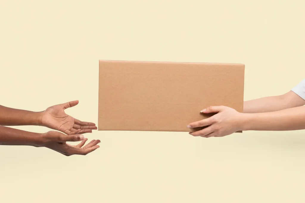 Imagem mostrando as mãos de duas pessoas trocando um pacote de papelão, simbolizando o ato de entrega ou frete.