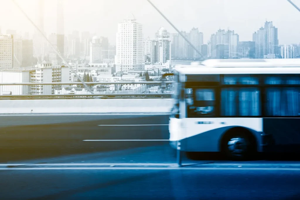Ônibus em movimento sobre uma ponte, com uma vista de cidade ao fundo, representando transporte urbano e a busca por soluções de mobilidade