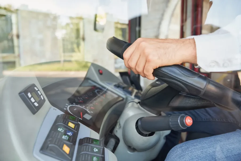 Mão de um motorista segurando o volante de um veículo de logística, com painel moderno e botões de controle visíveis.