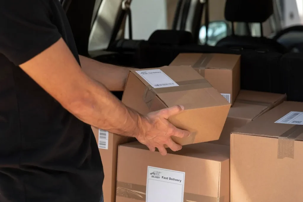Pessoa carregando uma caixa de papelão com etiqueta de entrega rápida, organizando pacotes dentro de um carro para transporte logístico.