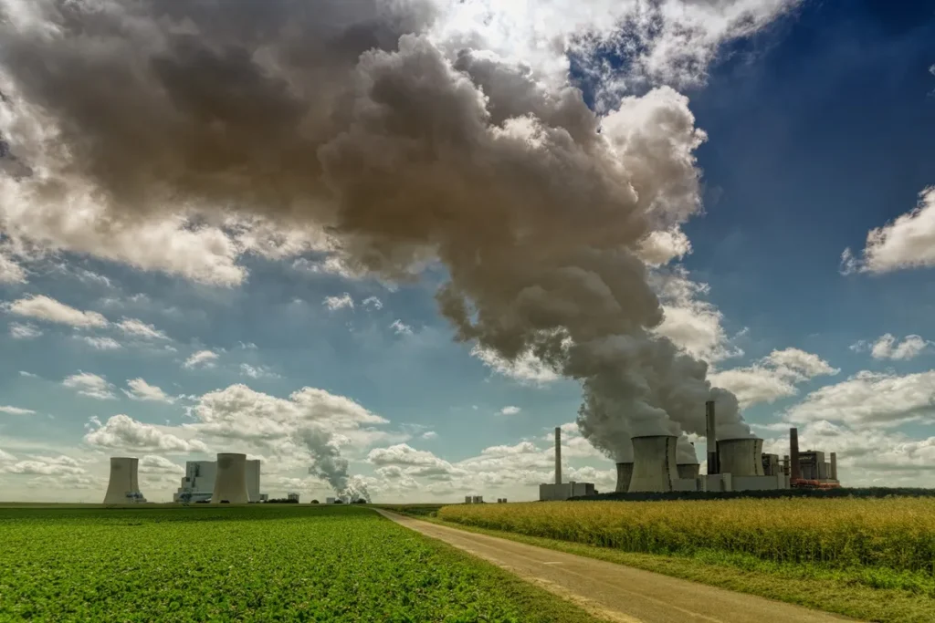 Usina de energia com grandes torres de resfriamento e emissão de fumaça em céu aberto, representando os impactos ambientais da poluição e emissão de carbono