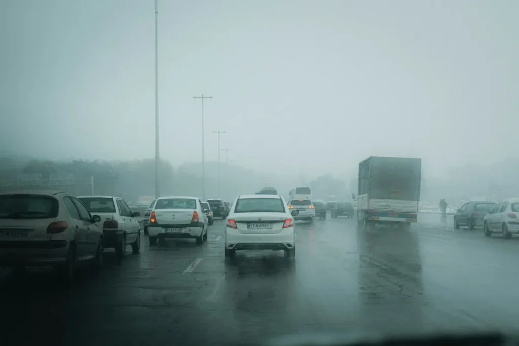 Carros em trânsito intenso sob forte neblina em uma estrada molhada
