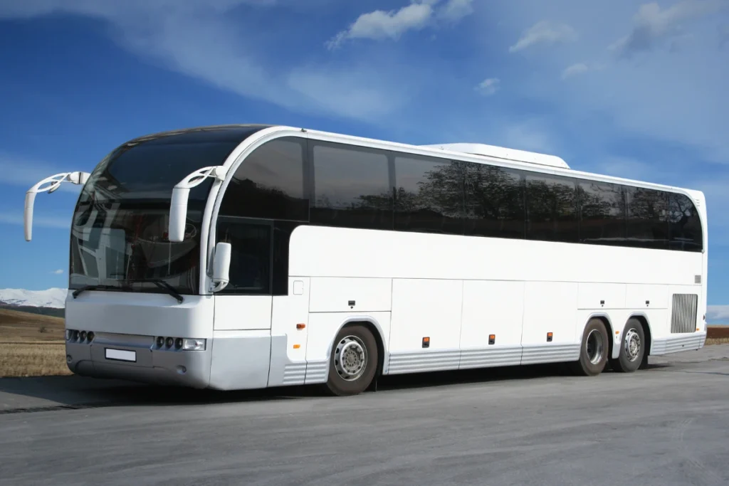 Ônibus executivo branco com janelas escurecidas estacionado numa estrada asfaltada, sob um céu azul com nuvens.