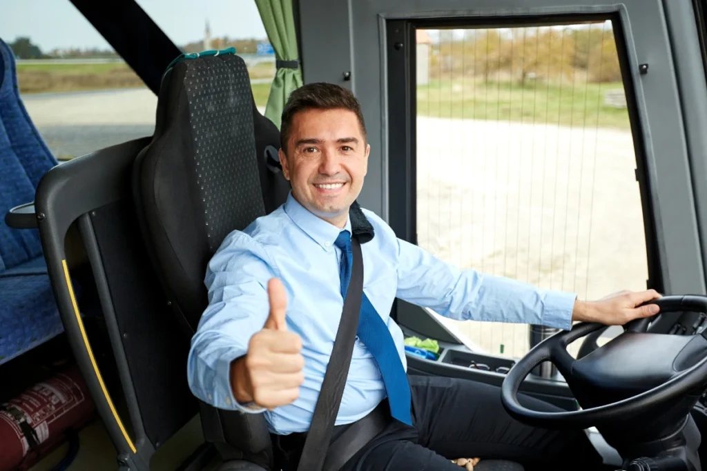 Ônibus de turismo branco estacionado em estrada asfaltada, com janelas escurecidas e céu azul com nuvens ao fundo