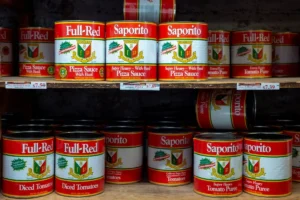 Fileira de garrafas de óleo de cozinha dourado da marca "Arawana Brand" (金龙鱼) em prateleiras de supermercado, com etiquetas verdes destacando seu uso em "óleo de soja". Um item comum entre os alimentos não perecíveis, essencial para o preparo de refeições. Descrição da Imagem: