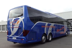 Ônibus de turismo azul da empresa Marcus Losert estacionado, com design moderno, três eixos e janelas escuras, em frente a um galpão
