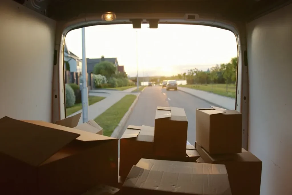 Interior de uma van de entrega repleta de caixas de papelão, com a visão de uma rua residencial ao pôr do sol, ilustrando o transporte de mercadorias em uma remessa expressa.