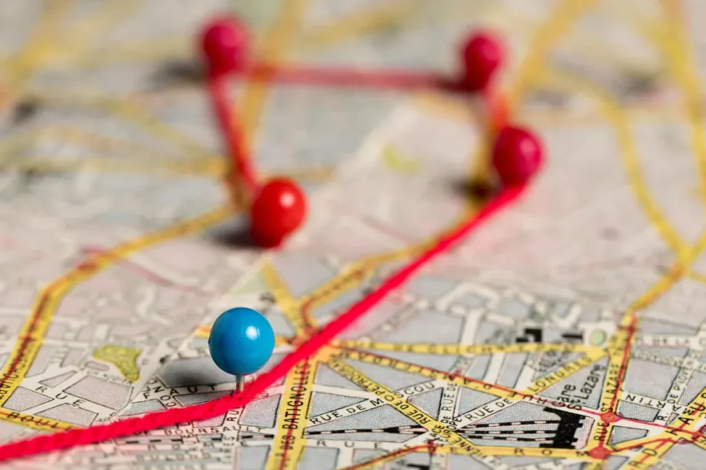 Um alfinete azul e um fio vermelho marcando uma rota em um mapa de papel de uma cidade, simbolizando o planejamento e a roteirização de viagens ou entregas.