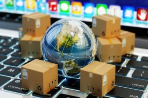 Globo terrestre cercado por caixas de encomendas sobre um teclado de computador, representando comércio internacional e e-commerce.