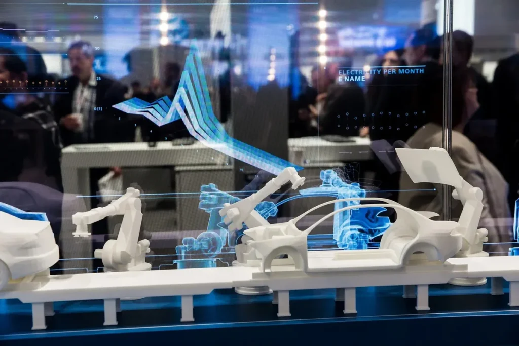 Modelo físico em escala de uma linha de montagem de automóveis e braços robóticos brancos. Sobre o modelo, há uma tela de realidade aumentada (AR) transparente que projeta gráficos de desempenho (gráfico de ondas azul e branco) e dados digitais, ilustrando o conceito de Digital Twins e a Indústria 4.0.