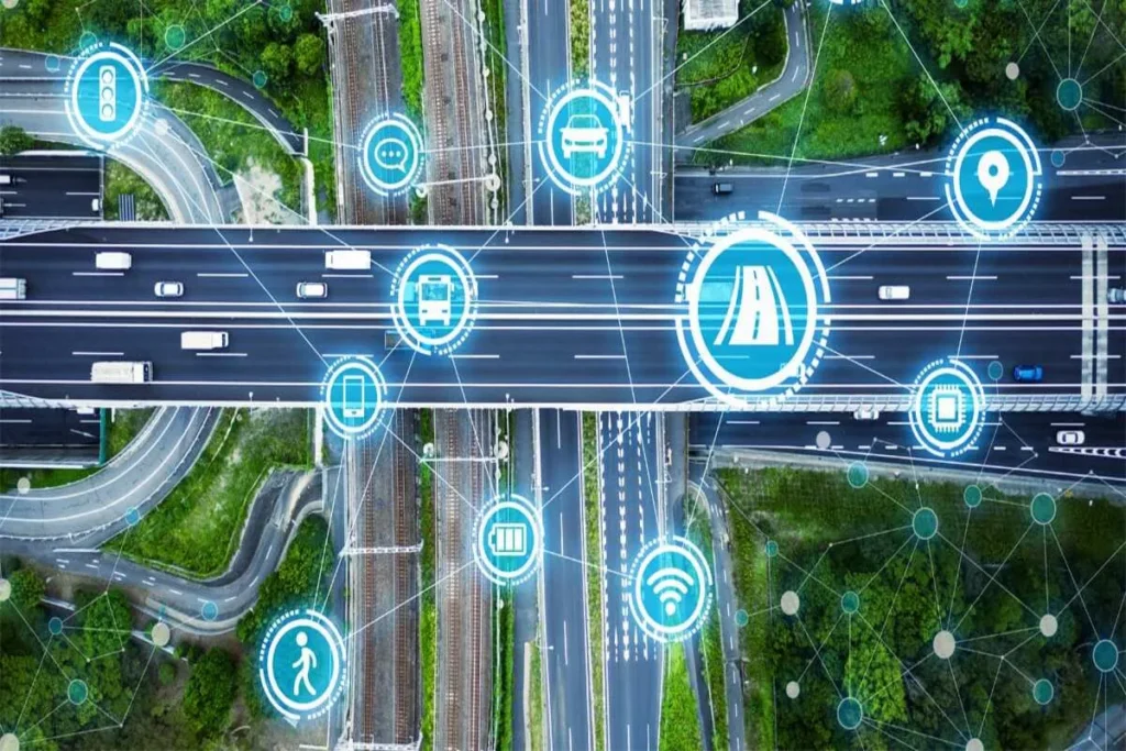 Vista aérea de uma complexa interseção de rodovias e linhas de trem, sobreposta com uma rede digital de ícones em néon azul, como carros, ônibus, WiFi e comunicação. A imagem ilustra o uso de Digital Twins para monitorar e otimizar a infraestrutura de transporte e o fluxo de dados em uma cidade inteligente.