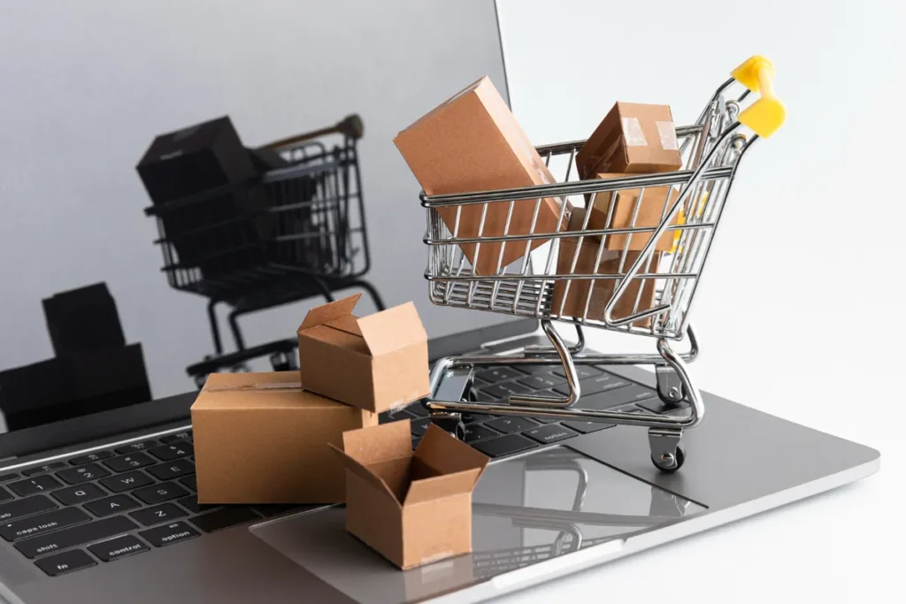Mini carrinho de compras cheio de pequenas caixas de remessa sobre um laptop, representando a gestão de pedidos e o dropshipping.