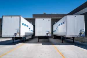Three white cargo trailers parked at an industrial shipping dock under clear blue skies.