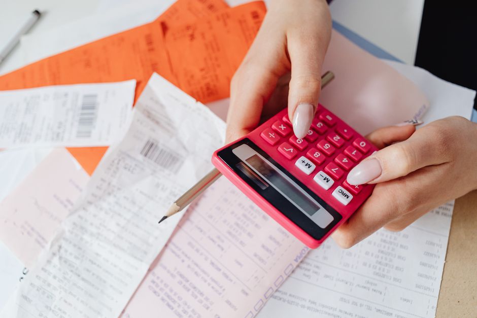 Pessoa calculando despesas com calculadora entre recibos e notas fiscais